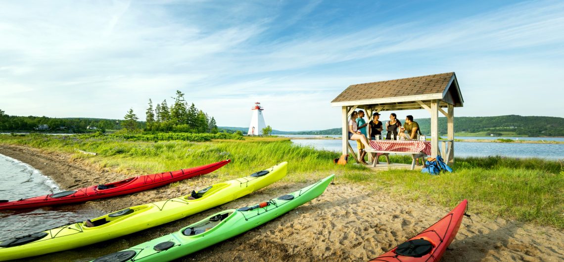 Kayaks on a sunny beach with a covered picnic spread.