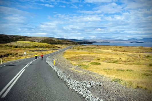2 cyclists riding along a deserted coastal road were the scenery is always superb and unobstructed by forests in south Iceland with Freewheeling Adventures.