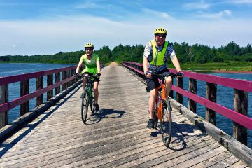 2 happy cyclists traversing a bridge along the traffic-free Confederation Trail, and bike paths of the National Park with Freewheeling Adventures.