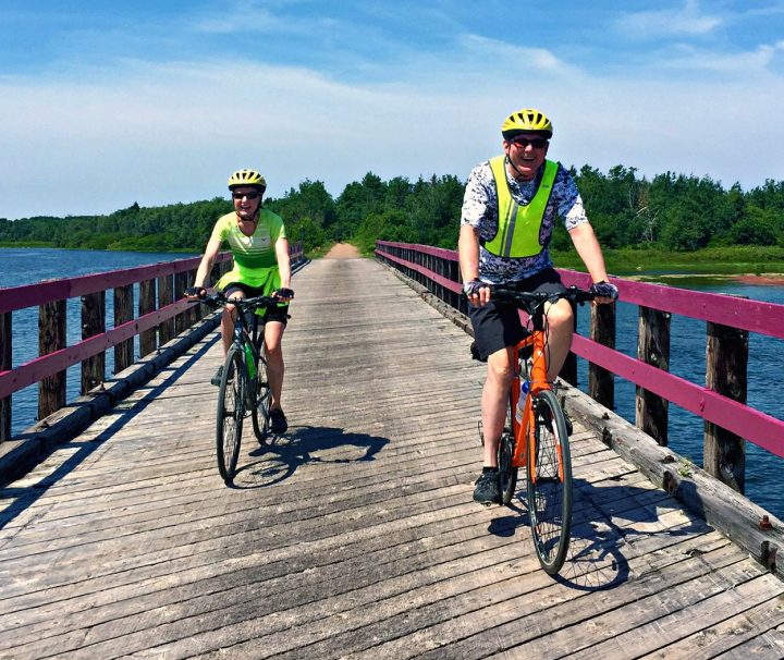 2 happy cyclists traversing a bridge along the traffic-free Confederation Trail, and bike paths of the National Park with Freewheeling Adventures.