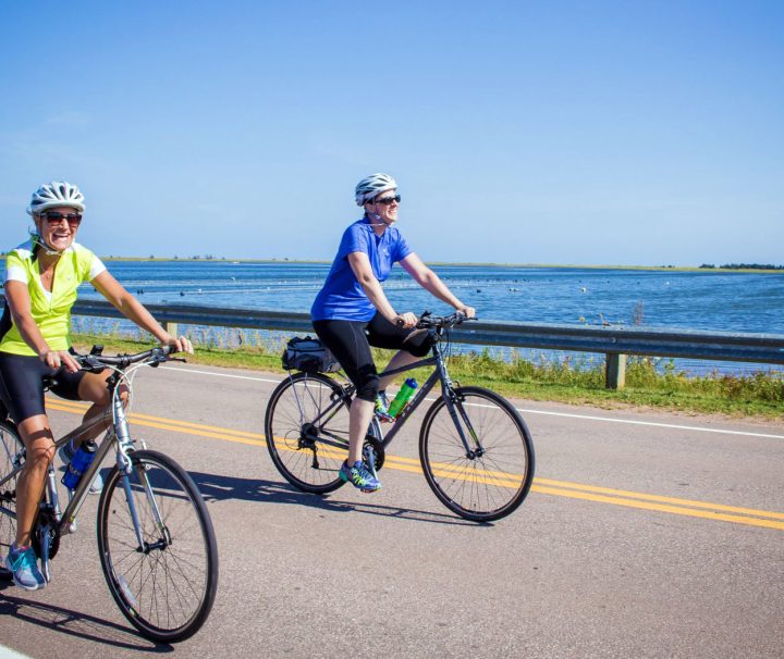 2 happy cyclists riding along one of Prince Edward Islands many stretches of low traffic coastal roads off the beaten path of the Confederation Trail.