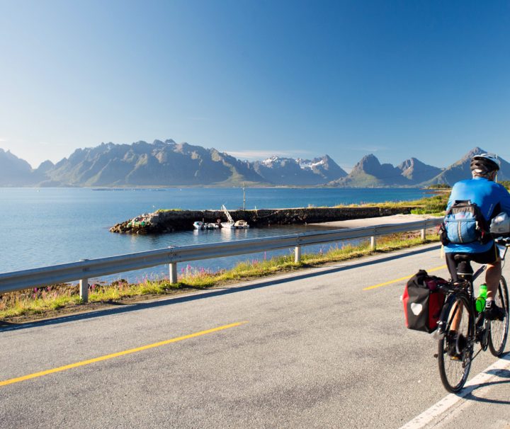 Cyclist riding away on a flat seaside road on tour with Freewheeling.