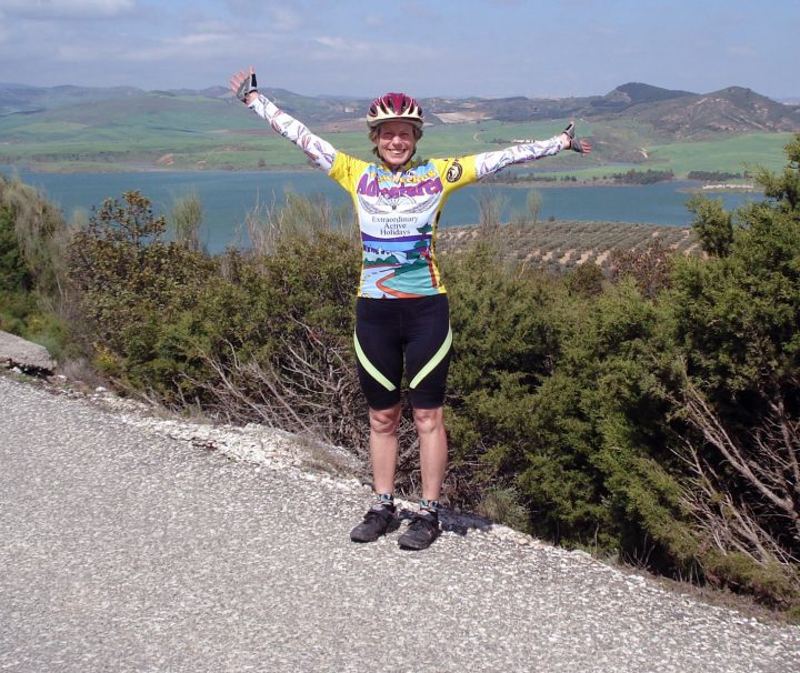 A cyclist full of joy with a mountain backdrop on a beautiful day on the challenging Spain: Andalucía Bike Tour with Freewheeling Adventures.