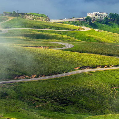 A scenic, winding mountain road known as a hairpin turn or switchback route, often found in hilly landscapes in the Pyrenees foothills