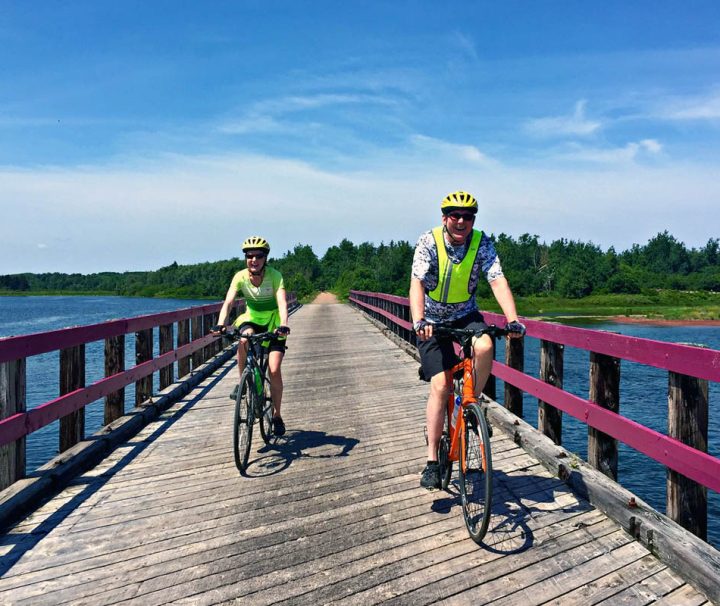 This image depicts a sunny day of cycling along the Confederation Trail in Prince Edward Island, likely near St. Peter's Bay, a popular route for tourists exploring the province by bicycle