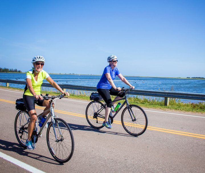 This image shows two individuals enjoying a scenic bicycle ride along a paved coastal side road of Prince Edward Island