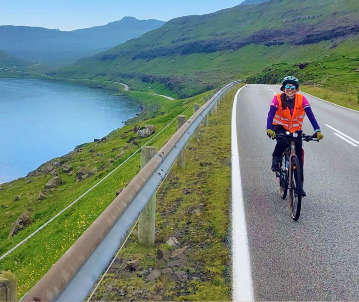 This image captures a moment of someone cycling on a scenic coastal road, in a mountainous region in the Faroe Islands