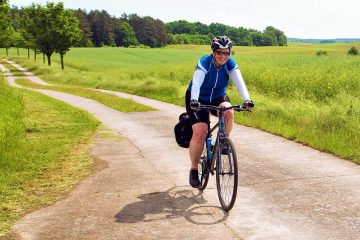 This image shows a person enjoying a bicycle tour along a scenic, paved path through a rural countryside between Berlin and Copenhagen