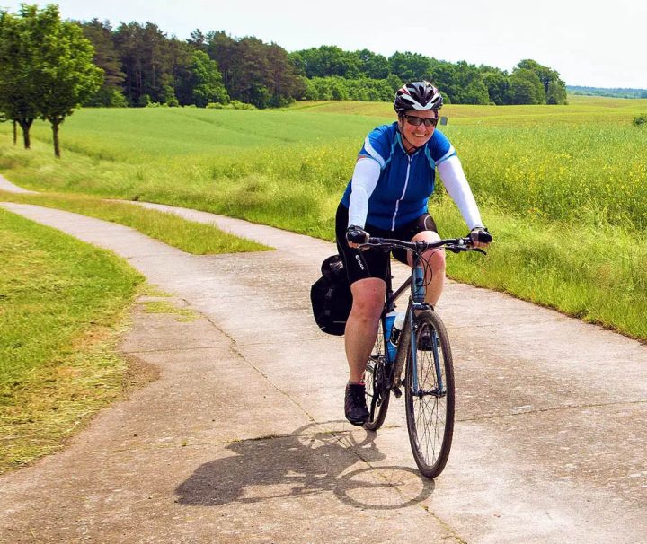 This image shows a person enjoying a bicycle tour along a scenic, paved path through a rural countryside between Berlin and Copenhagen