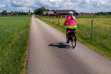 This image shows a person cycling on a paved rural path through the flat landscape of the Kattegattleden cycling route