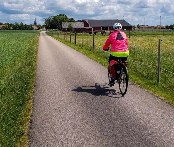 This image shows a person cycling on a paved rural path through the flat landscape of the Kattegattleden cycling route