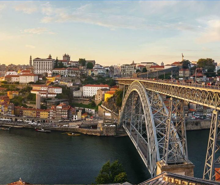 This image depicts a sunset view of the Dom Luís I Bridge in Porto, Portugal, a famous double-deck metal arch bridge spanning the Douro River
